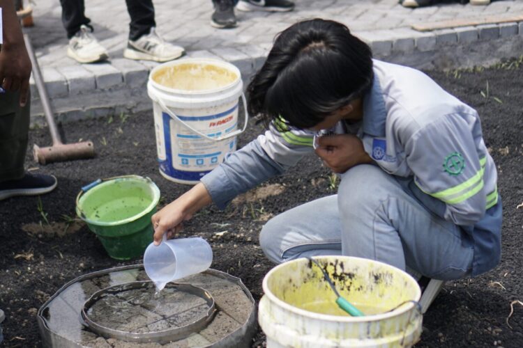 Salah satu mahasiswa ITS saat melakukan pengujian infiltrasi pada inovasi paving porous dari fly ash di Desa Sumberejo, Probolinggo. (Foto: Humas ITS/BS)