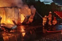 Petugas DPKP Surabaya berusaha menjinakkan apii yang membakar warung semi permanen. (Foto: Command Cenetr 112-Ist/BS)