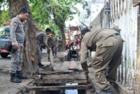 Mengembalikan fungsi dan perawatan drainase, petugas Satpol PP Surabaya menertibkan lapak padagang di Manukan yang berada diatas drainase. (Foto: Satpol PP Surabaya/Ist)